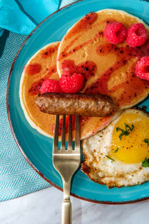 Pancake breakfast served with raspberry syrup with an egg and sausage to accompany