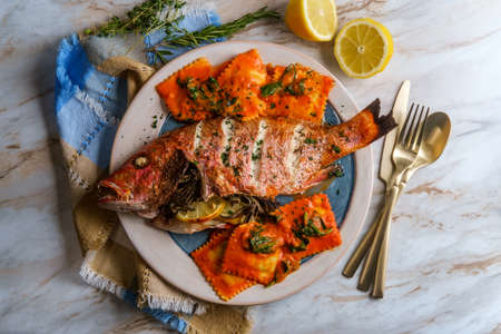 Whole head-on red snapper seafood dinner with ravioli in sherry wine pink sauceの写真素材