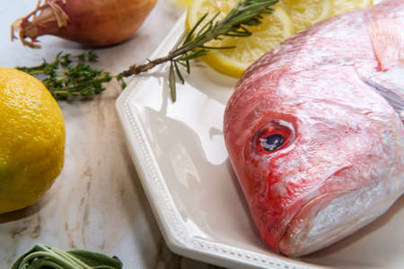 Fresh whole raw head-on red snapper with seasoning ingredientsの写真素材