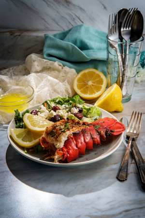 Grilled lobster tail served with fresh Greek salad with sliced lemon and melted butter for dippingの写真素材