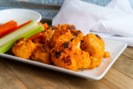 Vegetarian cauliflower buffalo wings served with blue cheese dipping sauce and sliced carrots and celeryの写真素材