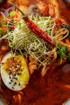 Korean kimchi ramen garnished with mushrooms scallions and a softboiled egg with black and white...
