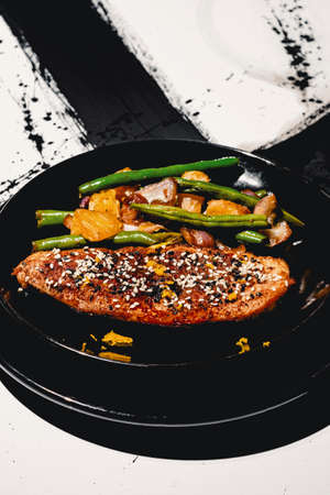 Chinese orange chicken garnished with tuxedo sesame seeds served with sauteed garlic green beans on abstract black and white background patternの写真素材