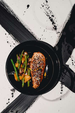 Chinese orange chicken garnished with tuxedo sesame seeds served with sauteed garlic green beans on abstract black and white background patternの写真素材