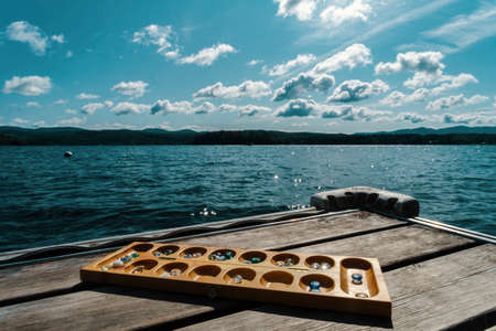 Traditional Mancala boardgame with glass pieces set up on dock by lake on summer day