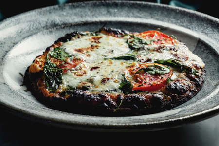 Mini personal pizza with sliced tomato and spinach roasted in brick fire ovenの写真素材