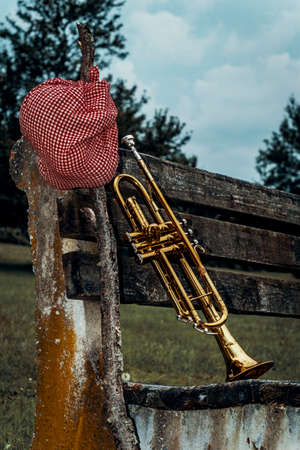 Traveling musicians trumpet and handkerchief picnic sack on a stick leaning against old park benchの写真素材