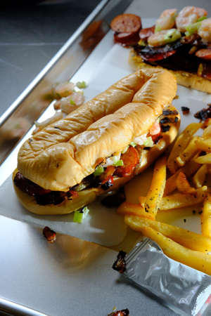Sausage onions and peppers hoagie sandwich topped with shrimp salad and served with side of friesの写真素材