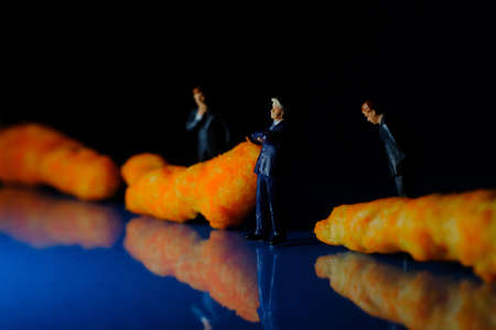 Miniature businessmen contemplating cheese puff unhealthy junk food snack macro closeupの写真素材