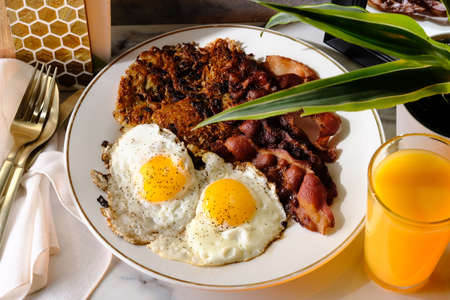 American breakfast two eggs sunny side up with bacon hash browns and a glass of fresh squeezed orange juiceの写真素材