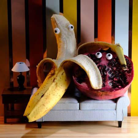 Silly banana and concerned pomegranate cuddling on the couchの写真素材