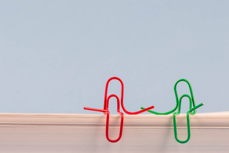 Paper clips red and green sitting on a white paper ream and talking or having a conversation. A photo with a copy space. Two paper clips who are friends talking or having a conversation or friendly talk. Ideal for back to school or office works.の写真素材