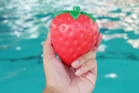 hand holding toy strawberry on swimming pool background