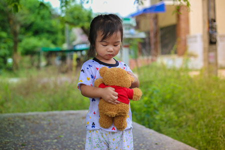 girl playing with bear doll under the tree and eating bananaの写真素材