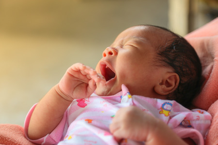 New born baby boy sleeping, yawning on mother's arm.の写真素材