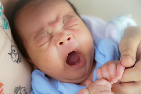 New born baby boy sleeping, yawning on mother's arm.の写真素材