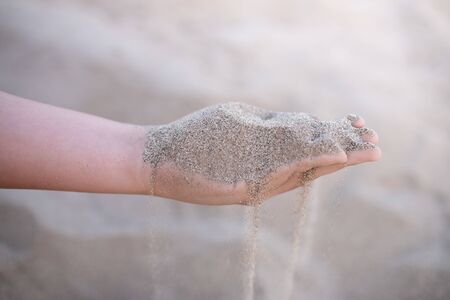 Sand puffs through the fingers of a girl's hand.の写真素材