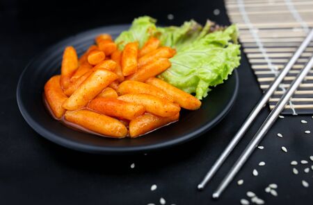 Spicy Tteokbokki on black crockery with metal chopstics.の写真素材