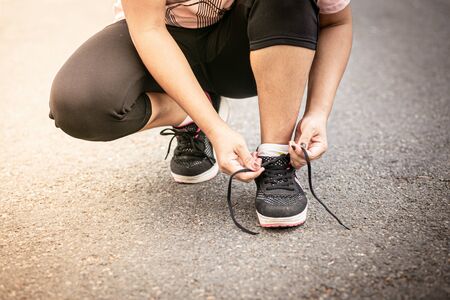 Cheerful runner sitting on floor on city streets. Woman tie shoelaces on road.の写真素材
