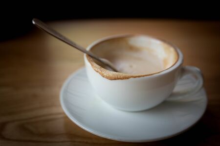 cup of hot coffee with milk foam on wooden table.
