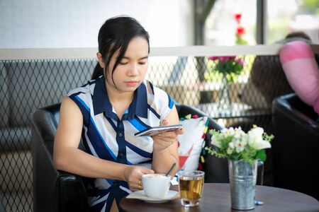 Beautiful woman sitting in a cafe, drinking coffee and using smartphone.の写真素材