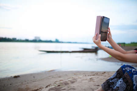 woman using tablet taking photo on beach.の写真素材