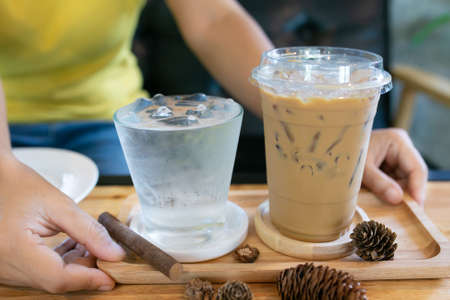 Glass of cool water and cool coffee on wooden table in coffee shop background.