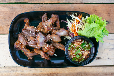 Grilled pork with sweet and sour sauce in black plate on wooden tableの写真素材