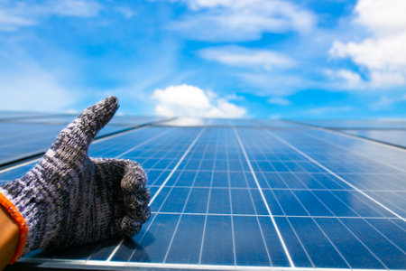 Hand in glove holding solar panel with blue sky and white clouds backgroundの写真素材
