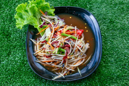 Green papaya salad in black plate on green grass background, Thai foodの写真素材