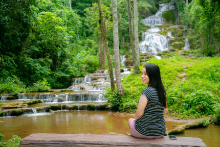 Beautiful asian woman sitting and looking at waterfall in the forest.の写真素材