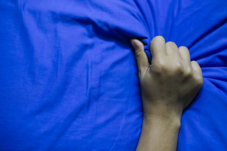 Hand of a man holding a pillow in the blue bed. Close up.の写真素材