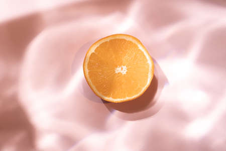 Fresh orange fruit on a pastel pink background with liquid water shadowの写真素材