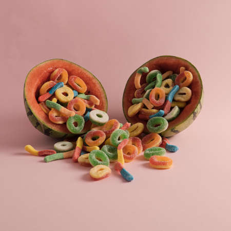 Watermelon halves filled with colorful jelly candies on a pastel pink backgroundの写真素材