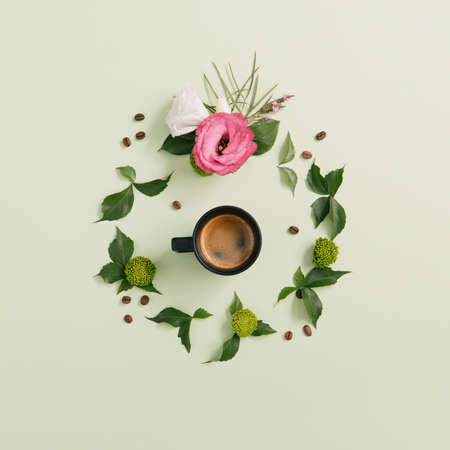 Espresso coffee cup with coffee beans and beautiful flowers with foliage on a pastel green backgroundの写真素材