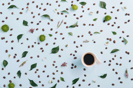 Coffee cup arranged with coffee beans flowers and green foliage on light blue background. Flat lay.の写真素材