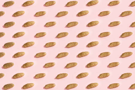 Gold color pine cones pattern on pale pink background. Creative concept. Autumn and festive minimal design.の写真素材