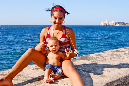 HAVANA, CUBA, MAY 11, 2009  A woman with her baby sitting on the edge of the wall of Malecon beach boulevard in Havana, Cuba, on May 11th, 2009  The Fort of Saint Charles in the background のeditorial素材