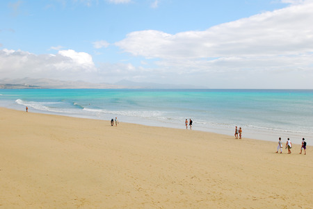 Fuerteventura, Canary Islands  People walking on a sand beach, with a view of the sea on a sunny day with mountains in the horizon  のeditorial素材