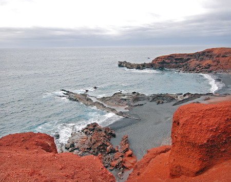 Lanzarote, Canary Islands  A rock in the sea that resembles a jetty, with red rock in the shore on a cloudy day の写真素材
