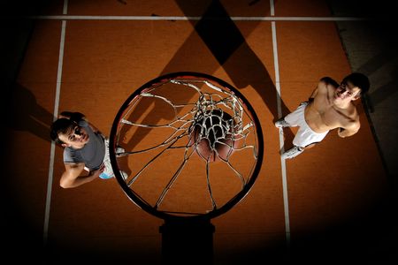 two mans is playing basketball in dark picture above basket