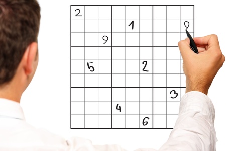 A close up of a male hand solving sudoku over white backgroundの写真素材