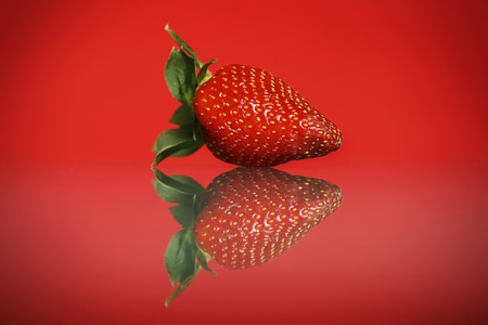 A picture of a fresh strawberry and it's reflection against red backgroundの写真素材