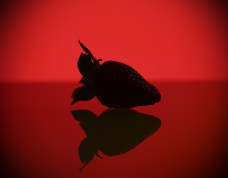A picture of a mysterious strawberry and it's reflection against red backgroundの写真素材