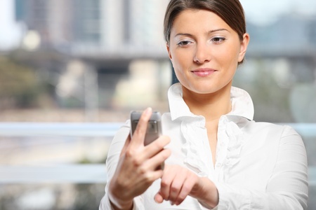 A portrait of a young pretty woman with her modern cellphone against light backgroundの写真素材