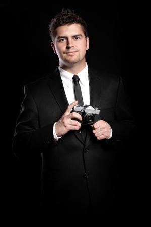 A portrait of an elegant young photographer holding a camera over black backgroundの写真素材