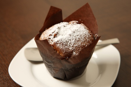 A picture of a chocolate muffin covered with icing sugar and served on a white plateの写真素材