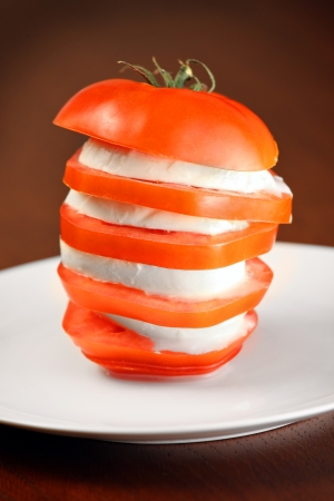 A picture of mozzarella cheese put in between tomato slices on a white plateの写真素材