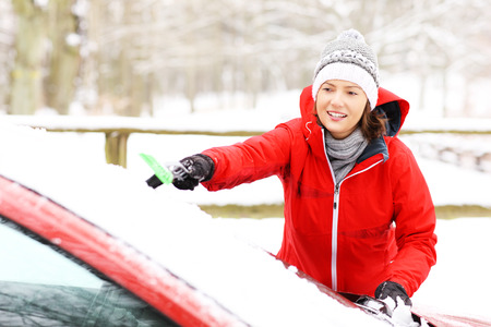 A picture of a young woman cleaning a windshield from the snowの写真素材