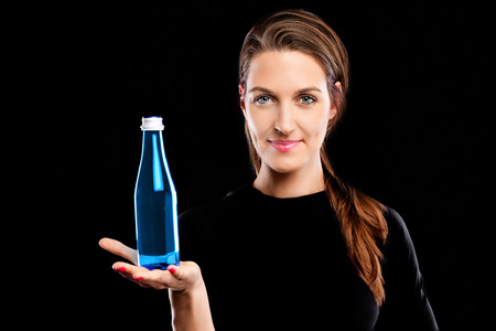 A picture of a young woman posing with a bottle of water over black backgroundの写真素材
